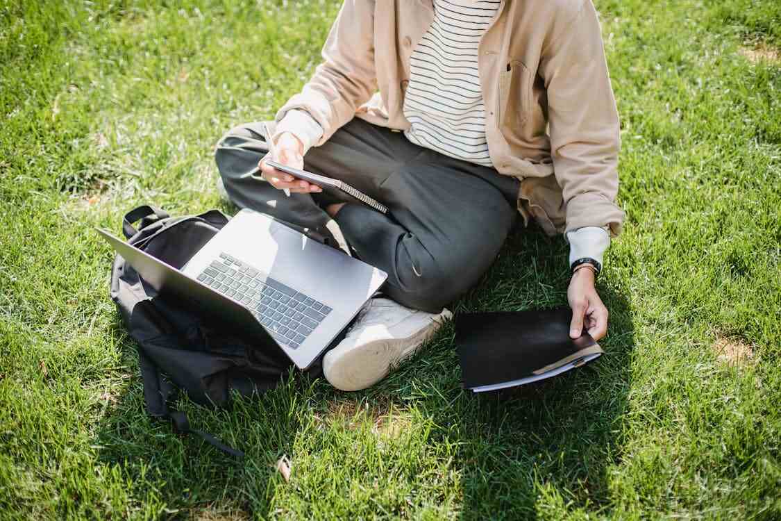 A student sitting on grass and researching back-to-school essentials on a laptop