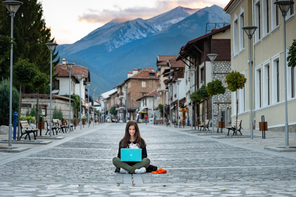 digital nomad on laptop sitting on a cobblestone road