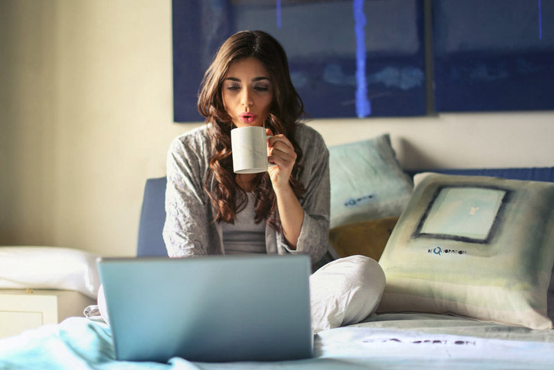 Female Student with a Mug Sits on Bed Using a Laptop