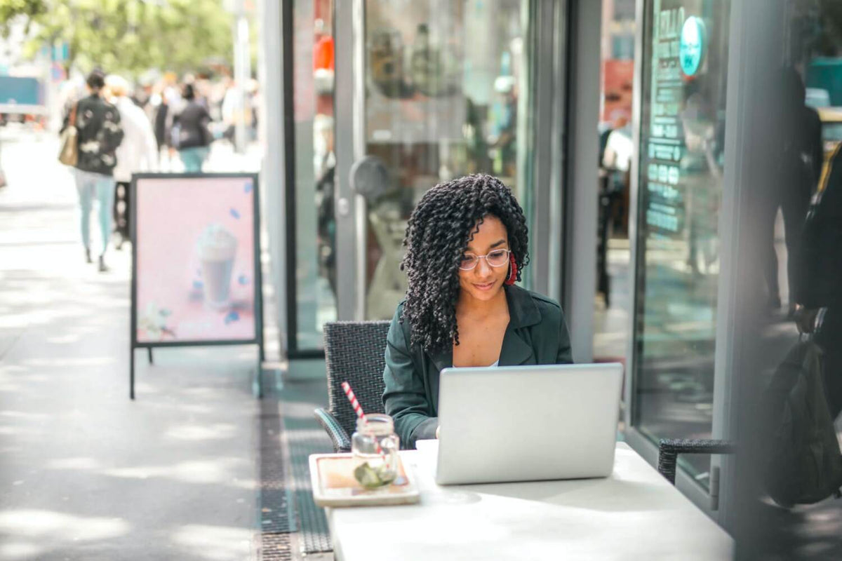 woman using laptop in an outdoor setting with a drink on the side