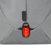 A close-up of a red bicycle tail light attached to the back of a gray backpack, with the brand name Targus