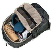 Open backpack with items including a blue mug, white device, and books on a black background