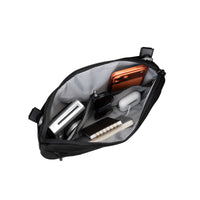 Black crossbody bag with compartments containing electronic devices on a white background