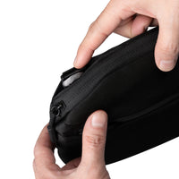 Black zippered pouch held by a hand on a white background