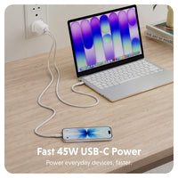 A white USB-C power cable shown plugged into a wall outlet, connected to a silver laptop and a smartphone on a light wood desk. White text at the bottom reads 'Fast 45W USB-C Power' and 'Power everyday devices, faster.
